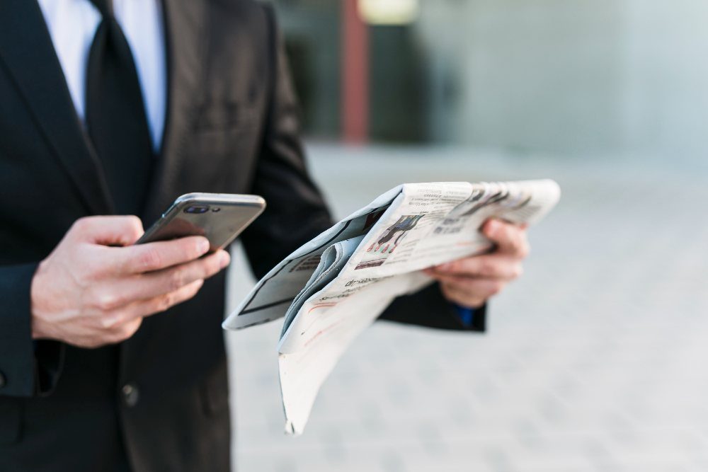 A person watching his mobile in one hand and holding a press release in other hand